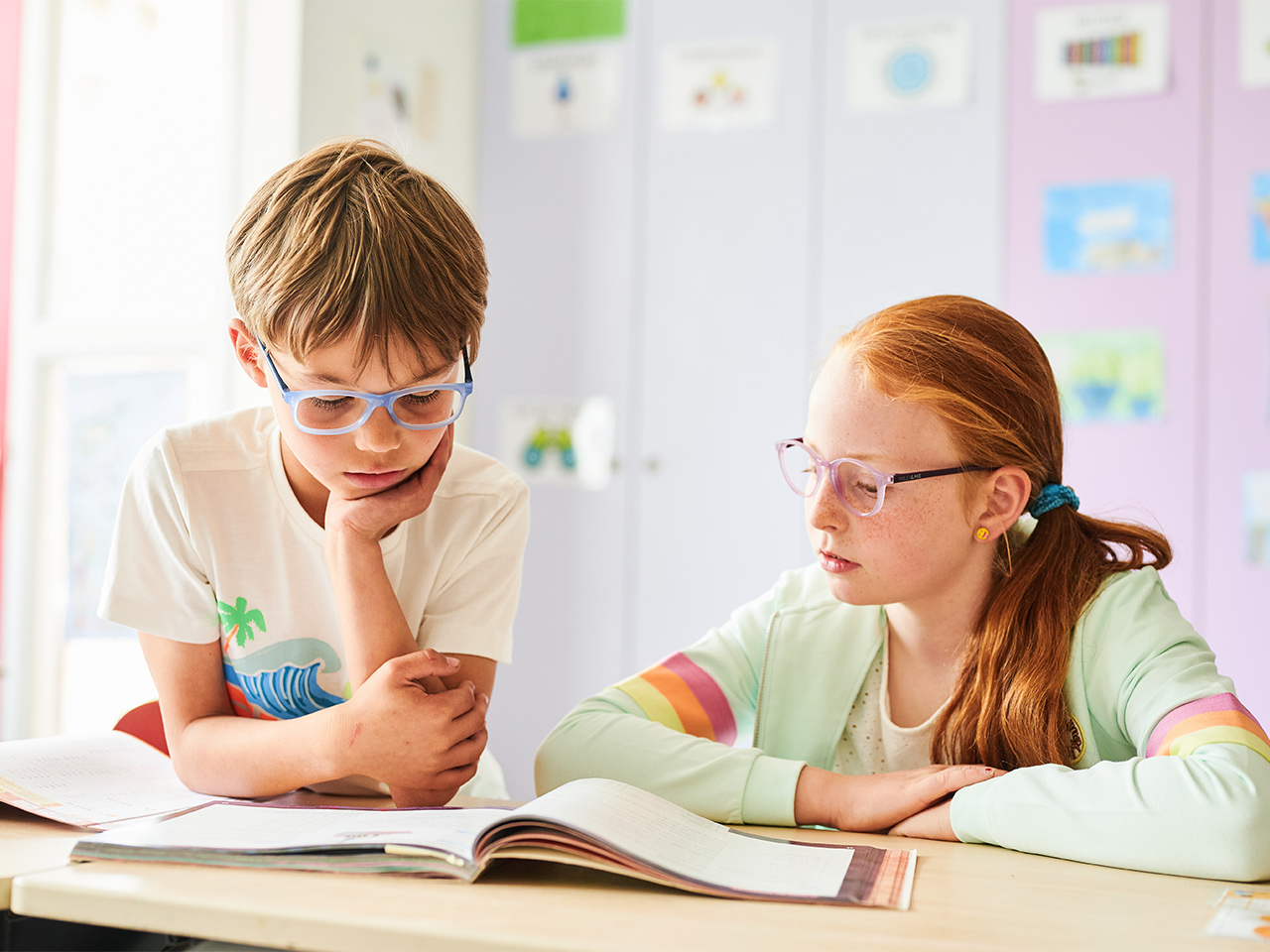 Zwei Kinder sitzen nebeneinander und lesen ein Buch an einem Tisch